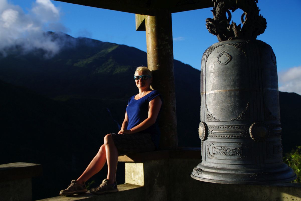 Turystka siedząca obok wielkiego, zdobionego dzwonu w Sapa.