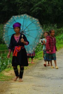 Starsza kobieta z plemienia Hmong z niebieskim parasolem i dzieci na ścieżce.